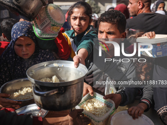 Palestinians gather to receive food cooked by a charity kitchen amid a hunger crisis as the Israel-Gaza conflict continues in Deir el-Balah,...