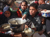 Palestinians gather to receive food cooked by a charity kitchen amid a hunger crisis as the Israel-Gaza conflict continues in Deir el-Balah,...