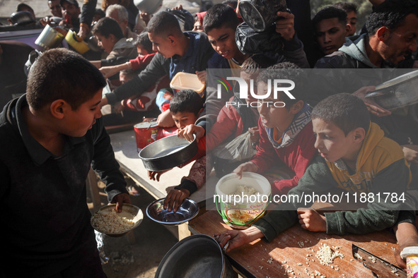 Palestinians gather to receive food cooked by a charity kitchen amid a hunger crisis as the Israel-Gaza conflict continues in Deir el-Balah,...