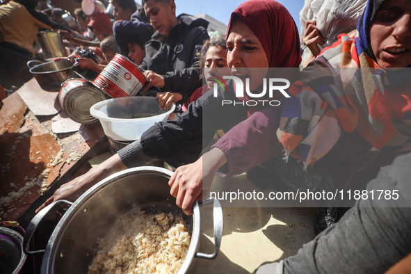 Palestinians gather to receive food cooked by a charity kitchen amid a hunger crisis as the Israel-Gaza conflict continues in Deir el-Balah,...