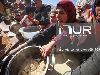 Palestinians gather to receive food cooked by a charity kitchen amid a hunger crisis as the Israel-Gaza conflict continues in Deir el-Balah,...