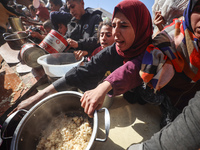 Palestinians gather to receive food cooked by a charity kitchen amid a hunger crisis as the Israel-Gaza conflict continues in Deir el-Balah,...