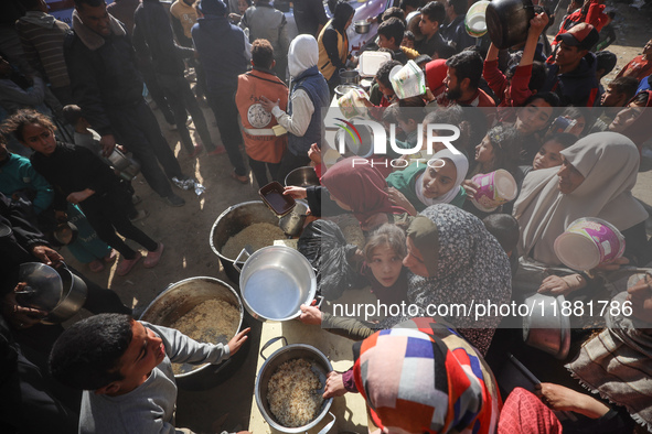 Palestinians gather to receive food cooked by a charity kitchen amid a hunger crisis as the Israel-Gaza conflict continues in Deir el-Balah,...