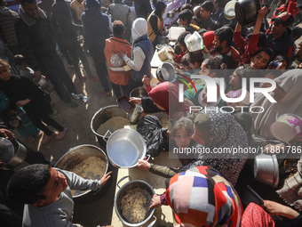 Palestinians gather to receive food cooked by a charity kitchen amid a hunger crisis as the Israel-Gaza conflict continues in Deir el-Balah,...