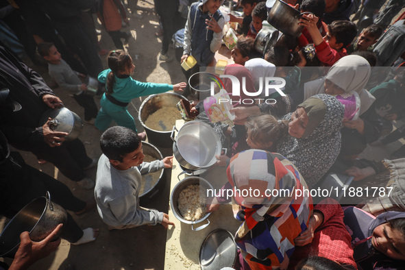 Palestinians gather to receive food cooked by a charity kitchen amid a hunger crisis as the Israel-Gaza conflict continues in Deir el-Balah,...