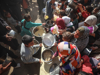 Palestinians gather to receive food cooked by a charity kitchen amid a hunger crisis as the Israel-Gaza conflict continues in Deir el-Balah,...