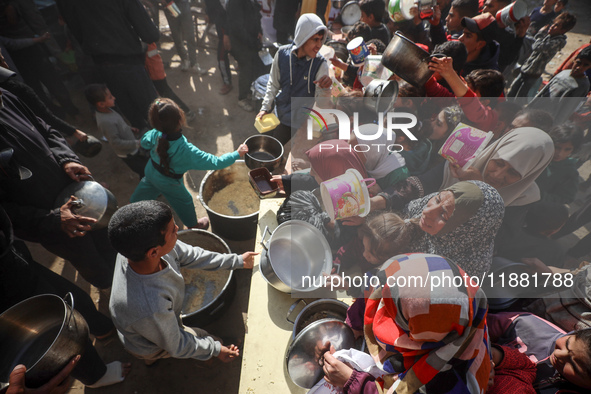 Palestinians gather to receive food cooked by a charity kitchen amid a hunger crisis as the Israel-Gaza conflict continues in Deir el-Balah,...