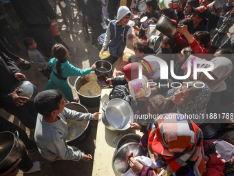 Palestinians gather to receive food cooked by a charity kitchen amid a hunger crisis as the Israel-Gaza conflict continues in Deir el-Balah,...