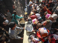 Palestinians gather to receive food cooked by a charity kitchen amid a hunger crisis as the Israel-Gaza conflict continues in Deir el-Balah,...