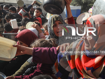 Palestinians gather to receive food cooked by a charity kitchen amid a hunger crisis as the Israel-Gaza conflict continues in Deir el-Balah,...