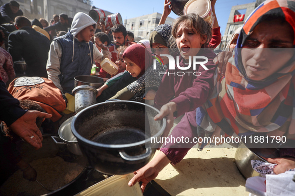 Palestinians gather to receive food cooked by a charity kitchen amid a hunger crisis as the Israel-Gaza conflict continues in Deir el-Balah,...