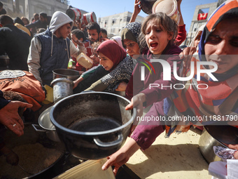 Palestinians gather to receive food cooked by a charity kitchen amid a hunger crisis as the Israel-Gaza conflict continues in Deir el-Balah,...