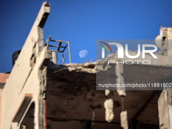 A general view shows the moon appearing behind a destroyed building in Deir al-Balah, on December 19, 2024, as the war between Israel and Ha...