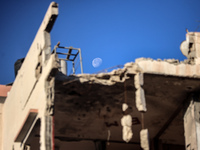 A general view shows the moon appearing behind a destroyed building in Deir al-Balah, on December 19, 2024, as the war between Israel and Ha...