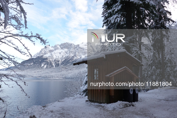 Waste bins under a wooden shelter in a snowy forest highlight local waste management efforts in a winter landscape in Grainau, Lake Eibsee,...