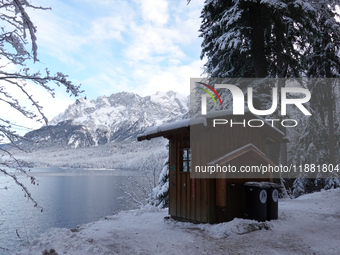 Waste bins under a wooden shelter in a snowy forest highlight local waste management efforts in a winter landscape in Grainau, Lake Eibsee,...