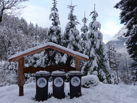 Waste bins under a wooden shelter in a snowy forest highlight local waste management efforts in a winter landscape in Grainau, Lake Eibsee,...