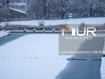 In Gauting, Bavaria, Germany, on January 6, 2021, the public swimming pool is blanketed in snow, with a red slide and surrounding trees crea...