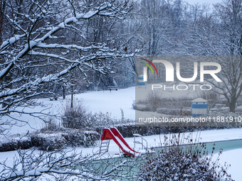 In Gauting, Bavaria, Germany, on January 6, 2021, the public swimming pool is blanketed in snow, with a red slide and surrounding trees crea...