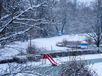 In Gauting, Bavaria, Germany, on January 6, 2021, the public swimming pool is blanketed in snow, with a red slide and surrounding trees crea...