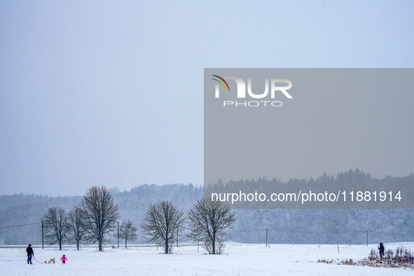 In Gauting, Bavaria, Germany, on January 6, 2021, a family with a sled spends a snowy day outdoors, with a child playing in a snow-covered f...