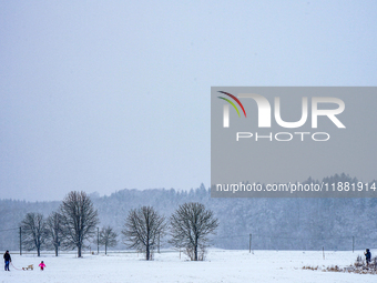 In Gauting, Bavaria, Germany, on January 6, 2021, a family with a sled spends a snowy day outdoors, with a child playing in a snow-covered f...