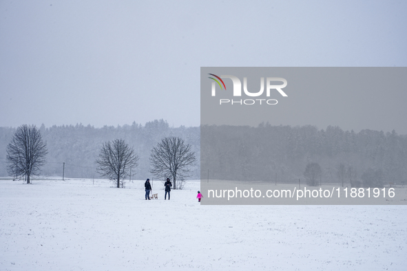 In Gauting, Bavaria, Germany, on January 6, 2021, a family spends a snowy day outdoors, with a child playing in a snow-covered field while t...