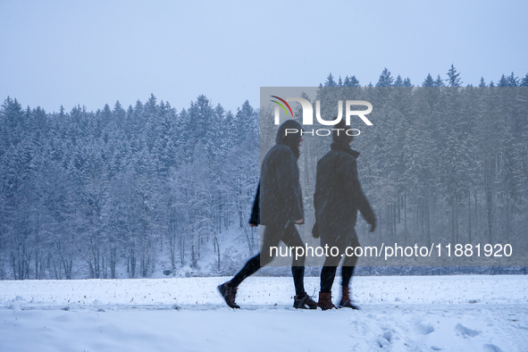 In Gauting, Bavaria, Germany, on January 6, 2021, two people walk through a snow-covered landscape during a snowfall, with a forest backdrop...