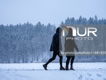 In Gauting, Bavaria, Germany, on January 6, 2021, two people walk through a snow-covered landscape during a snowfall, with a forest backdrop...