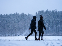 In Gauting, Bavaria, Germany, on January 6, 2021, two people walk through a snow-covered landscape during a snowfall, with a forest backdrop...