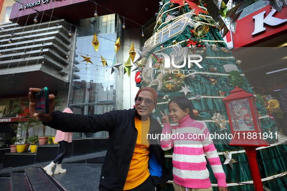 People take a selfie in front of an artificial Christmas tree set at the entrance of a mall in Kathmandu, Nepal, on December 19, 2024, ahead...