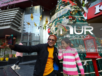 People take a selfie in front of an artificial Christmas tree set at the entrance of a mall in Kathmandu, Nepal, on December 19, 2024, ahead...