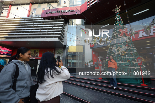 Nepali girls pose and take photos in front of an artificial Christmas tree set at the entrance of a mall in Kathmandu, Nepal, on December 19...