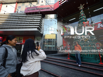 Nepali girls pose and take photos in front of an artificial Christmas tree set at the entrance of a mall in Kathmandu, Nepal, on December 19...