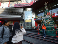 Nepali girls pose and take photos in front of an artificial Christmas tree set at the entrance of a mall in Kathmandu, Nepal, on December 19...