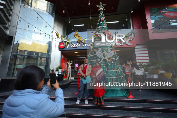 A Nepali couple poses and takes photos in front of an artificial Christmas tree set at the entrance of a mall in Kathmandu, Nepal, on Decemb...