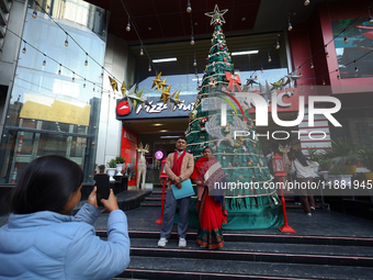 A Nepali couple poses and takes photos in front of an artificial Christmas tree set at the entrance of a mall in Kathmandu, Nepal, on Decemb...