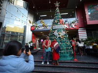 A Nepali couple poses and takes photos in front of an artificial Christmas tree set at the entrance of a mall in Kathmandu, Nepal, on Decemb...