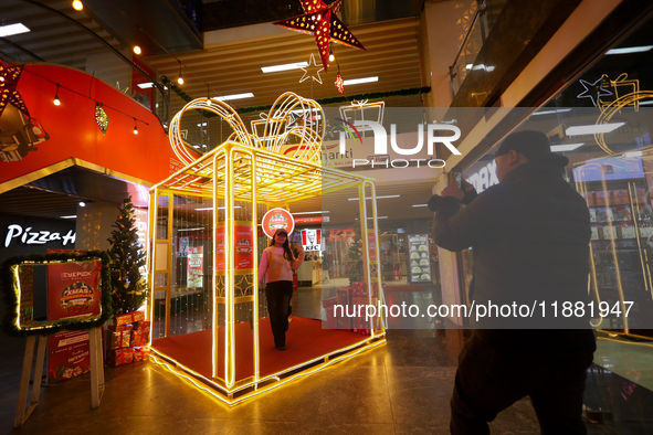 A Nepali couple poses and takes photos in front of an artificial Christmas tree set at the entrance of a mall in Kathmandu, Nepal, on Decemb...