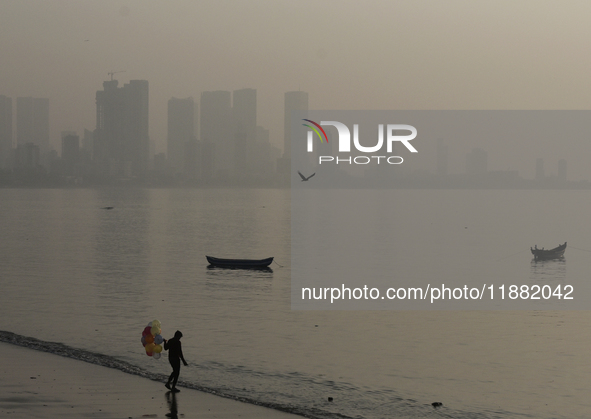 A balloon seller stands near a sea beach with a backdrop of the cityscape, which is covered with smog, in Mumbai, India, on December 19, 202...