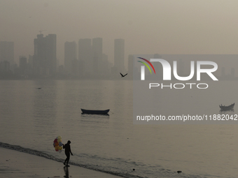 A balloon seller stands near a sea beach with a backdrop of the cityscape, which is covered with smog, in Mumbai, India, on December 19, 202...