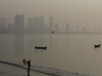 A balloon seller stands near a sea beach with a backdrop of the cityscape, which is covered with smog, in Mumbai, India, on December 19, 202...