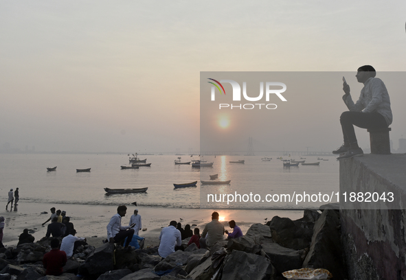 People enjoy the sunset on a beach in Mumbai, India, on December 19, 2024. 