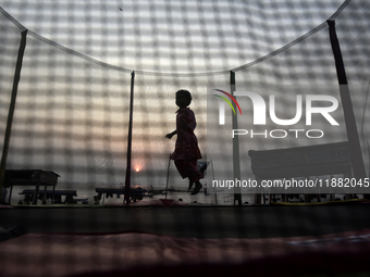 A child jumps on a round trampoline with an enclosure net near a sea beach in Mumbai, India, on December 19, 2024. (