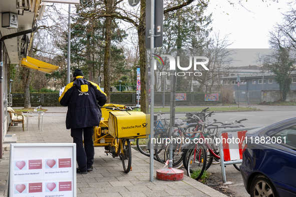 In Munich, Bavaria, Germany, on December 19, 2024, a Deutsche Post postman delivers letters to a residential building, with his yellow deliv...