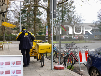 In Munich, Bavaria, Germany, on December 19, 2024, a Deutsche Post postman delivers letters to a residential building, with his yellow deliv...