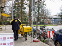 In Munich, Bavaria, Germany, on December 19, 2024, a Deutsche Post postman delivers letters to a residential building, with his yellow deliv...