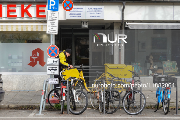 In Munich, Bavaria, Germany, on December 19, 2024, a Deutsche Post postman delivers letters to a residential building, with his yellow deliv...