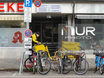 In Munich, Bavaria, Germany, on December 19, 2024, a Deutsche Post postman delivers letters to a residential building, with his yellow deliv...