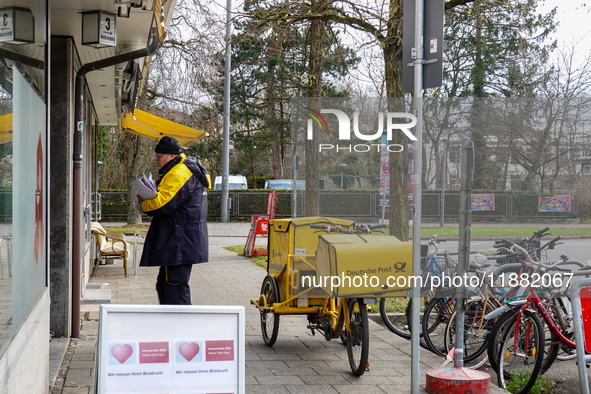 In Munich, Bavaria, Germany, on December 19, 2024, a Deutsche Post postman delivers letters to a residential building, with his yellow deliv...